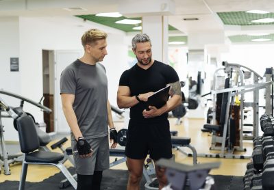Un sporitf discute avec un coach sportif de plus de 30 ans en salle de sport